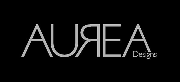 The image features a logo with the text "AUREA Designs." The word "AUREA" is written in large, uppercase, gray letters with a sleek, modern font. The word "Designs" is written in smaller, uppercase gray letters and is positioned in the bottom right corner, aligned with the "A" in "AUREA." The background of the logo is black, which contrasts sharply with the gray text, making it stand out.